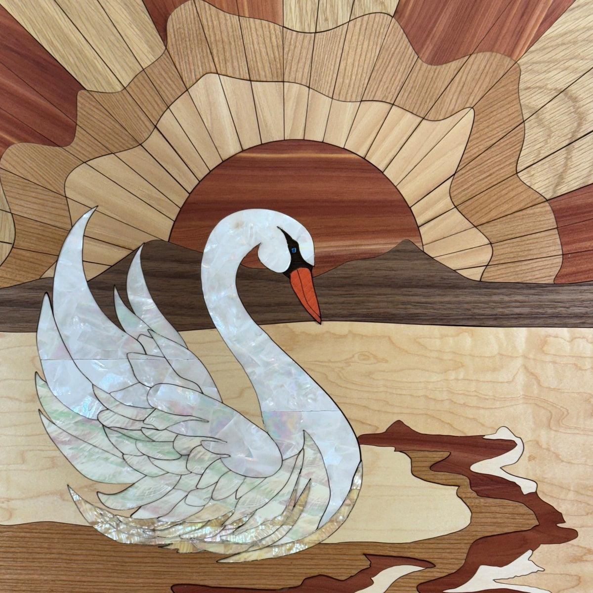 A square wooden art piece featuring an inlaid white swan with an orange beak against a sunburst and mountain background, mounted on a black wire display grid with two small labels below.