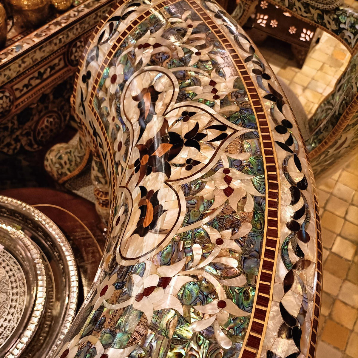 An ornate curved bench or sofa featuring intricate inlay work with mother-of-pearl floral motifs in shades of green, black, white, and gold, set against a tiled background.